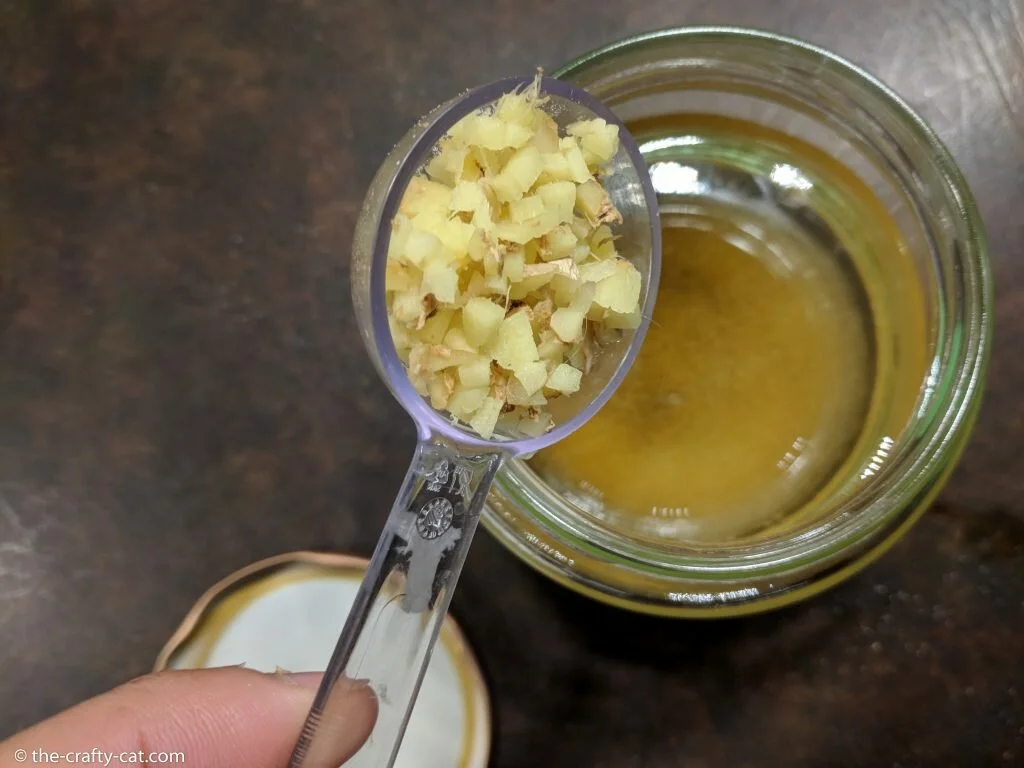 a jar with a ginger bug and a spoon of chopped ginger being poured in