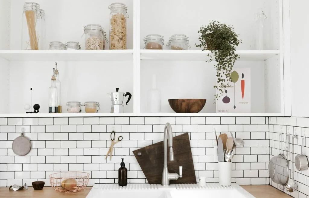 a white kitchen that is plastic free filled with mason jars with food, a sink and a kitchen shelf