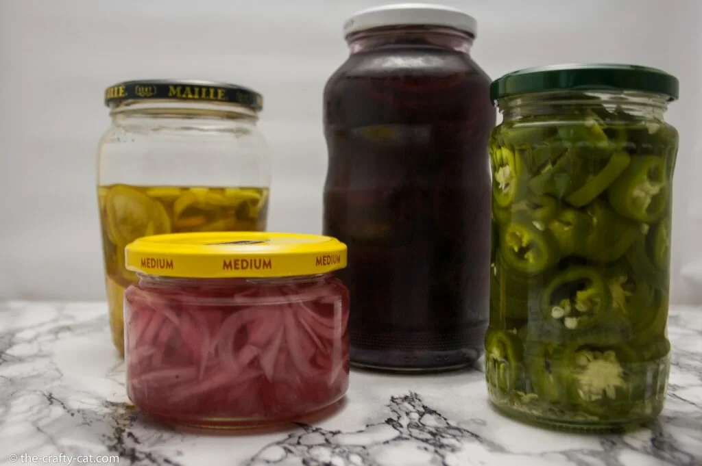 a row of pickled vegetables in mason jars. Turmeric cucumbers, pickled red onions, pickled jalapenos and pickled beets